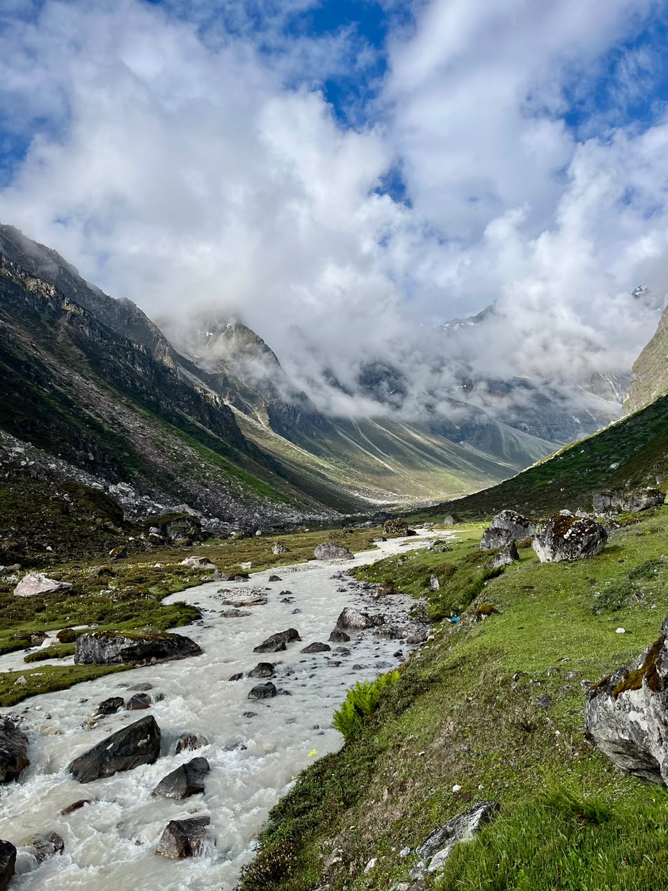 A glacial river running through a wide valley floor, clouds over the surrounding peaks