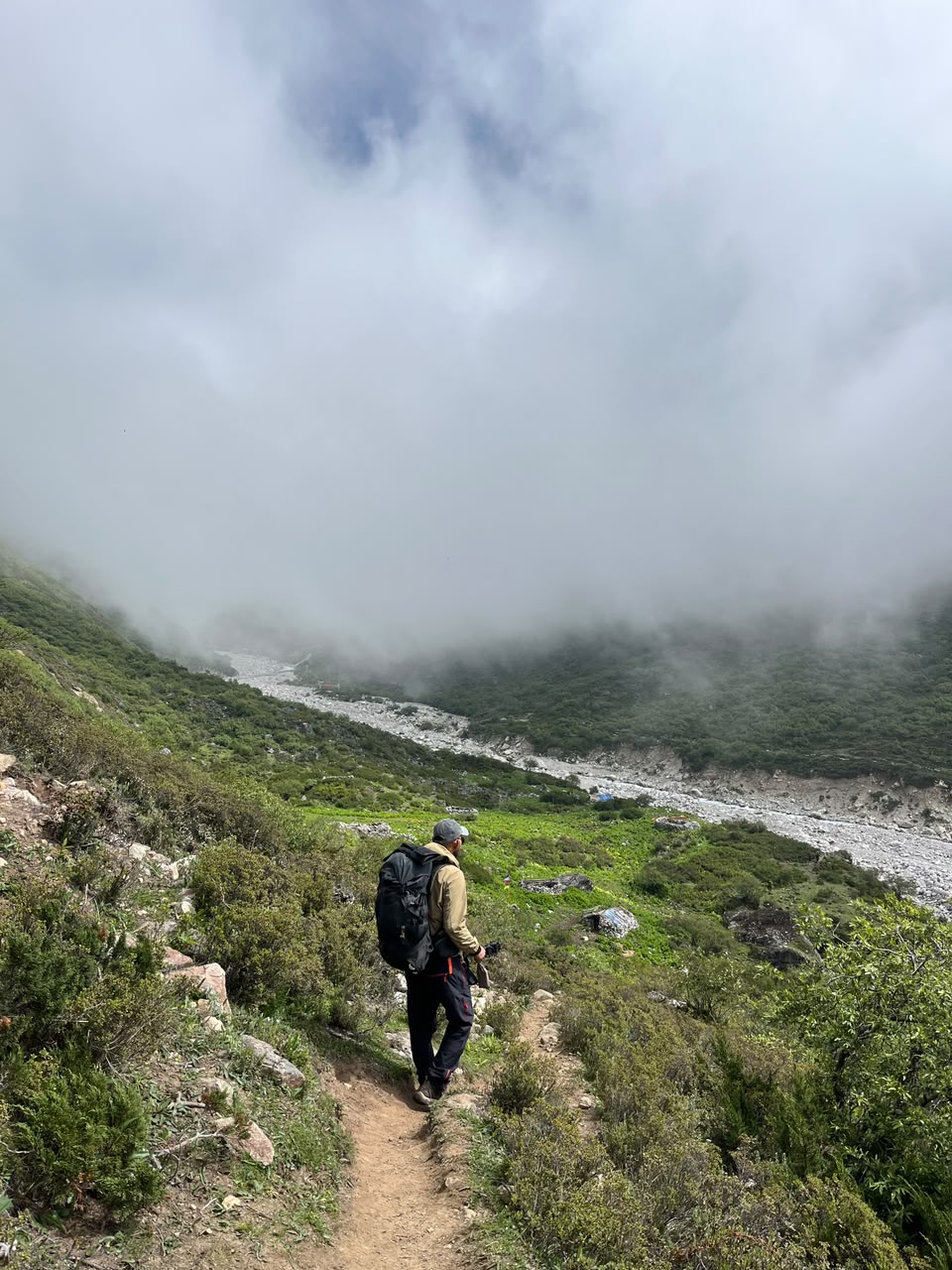 A hiker descending a grassy trail into a cloud-filled valley, river visible below