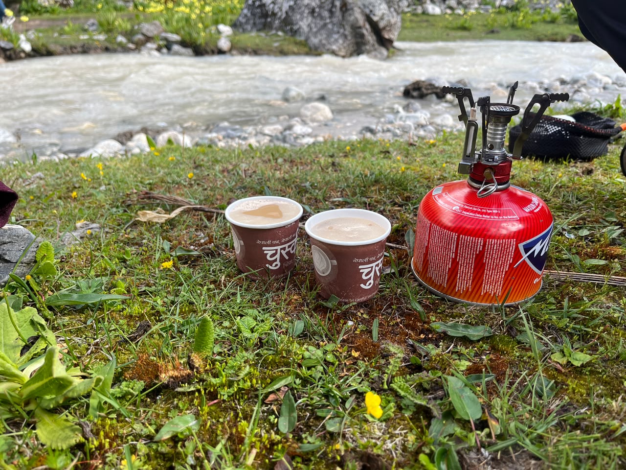 Two cups of milk tea by a glacial stream, camp stove beside them